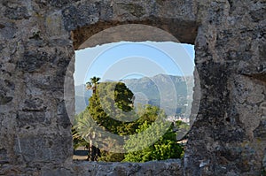 Old stone wall window overlook alley of palm trees. Mountains in the background