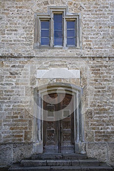 Old stone wall with windows, stairs a massive wooden door and a blank sign