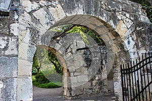 Old stone walls and archways with trees and vines and hanging lanterns and a wrong iron gate