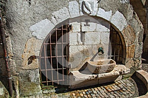 Old stone water fountain with iron gates and heraldic shield on the arch in Annecy.