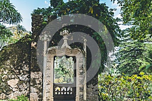 Old stone weathered gate with moss on the wall and metal door in a park.