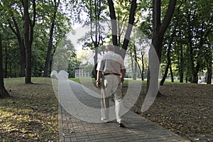 An old, stooped man walks sullenly and alone along the path in the park with a gray umbrella instead of a cane photo