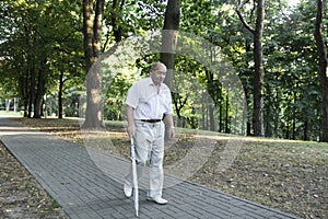 An old, stooped man walks sullenly and alone along the path in the park with a gray umbrella instead of a cane photo