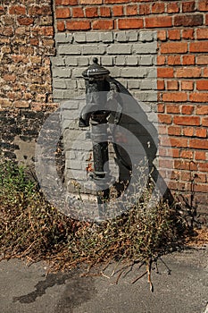 Old street water pump made in iron in front of a brick wall at the city of Bruges.