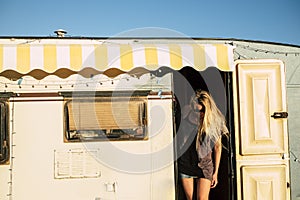 Old style american concept with beautiful blonde young girl on the door of a vintage old caravan - diversity and alternative