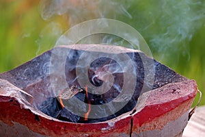 An old style brazier with hot coal and smoke in outdoor, blurred green nature background