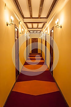 Old style hotel hallway with wooden brown doors, reddish carpet, and yellow walls