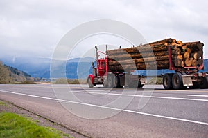 Old style red big rig semi truck transporting long logs on spectacular road in Columbia Gorge area