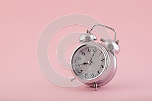 Old style silver alarm clock on pink background