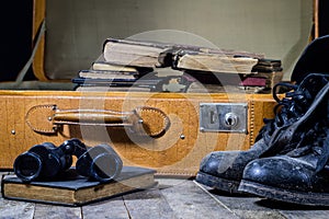 Old stylish suitcase. Military muddy shoes on a suitcase. Suitcase on a wooden table.