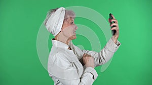 Old stylish woman is talking for video chat using mobile phoneisolated over green background. Profile