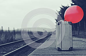 Old suitcase with a red balloon at the train station with retro effect