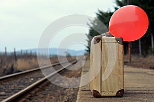 Old suitcase with a red balloon at the train station with retro effect