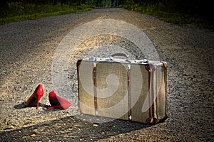 Old suitcase with red shoes left on road