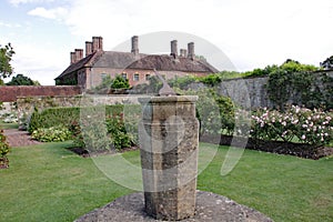 Old sundial on top of a brick plinth, in front of an English country house