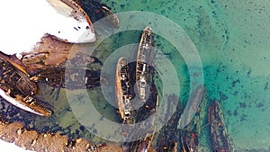 Old sunken ships near coast in winter. Footage. Top view of graveyard of ships in turquoise water off snowy coast in