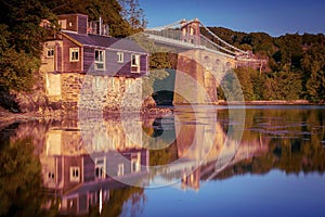 Old suspension bridge and a building reflecting on the water of Menai Straits