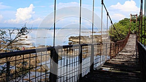 Old suspension bridge on the rocks beach, dull iron fences, broken wooden footings