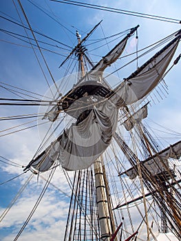 Old Tall Ship Sail, Mast, and Riggings Against Blue Sky