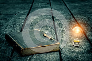 Old tattered book on a wooden table. Reading by candlelight. Vintage composition. Ancient library.