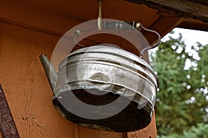 Old tea kettle hangs from a garage overhang photo