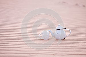 Old teapot and cup in sahara sand dune