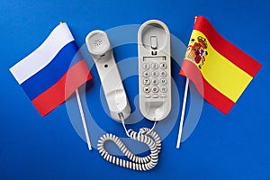 Old telephone and flags of Russia and Spain on a blue background, concept on the theme of telephone conversations between