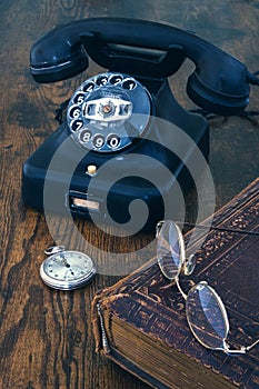 Old telephone, pocket watch, book andd glasses on wooden table