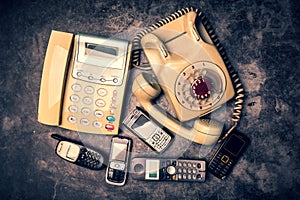 Old telephone with rotary dial, landline and obsoleted cellphone on a grunge background