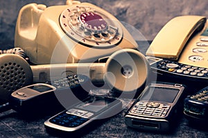 Old telephone with rotary dial, landline and obsoleted cellphone on a grunge background