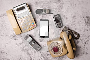 An old telephone with rotary dial, a landline, an obsoleted cellphone and smartphone on a grunge background