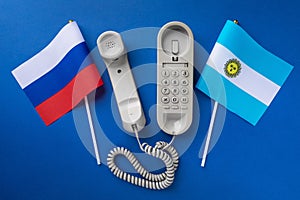 Old telephone and two flags on a blue background, concept on the theme of telephone conversations between Argentina and Russia