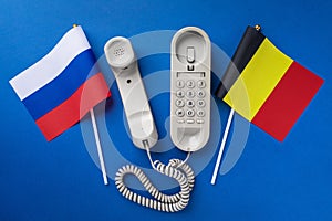 Old telephone and two flags on a blue background, concept on the theme of telephone conversations between Belgium and Russia