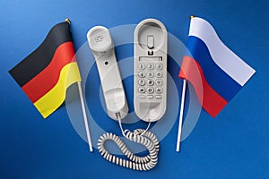 Old telephone and two flags on a blue background, concept on the theme of telephone conversations between Germany and Russia