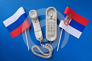 Old telephone and two flags on a blue background, concept on the theme of telephone conversations between Serbia and Russia