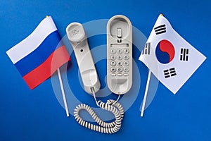 Old telephone and two flags on a blue background, concept on the theme of telephone conversations between South Korea and Russia