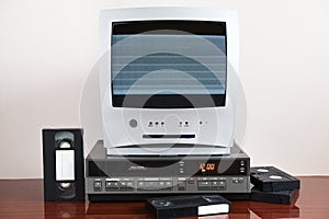 An old television set with static on the screen with a built-in DVD player and a vintage VCR standing next to it.