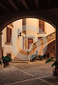 Old terracotta colored courtyard with a large staircase seen through a dark archway in a residential neighborhood in Palma