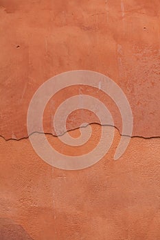 Old terracotta painted stucco wall with cracked plaster. Background texture