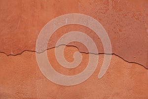 Old terracotta painted stucco wall with cracked plaster. Background texture