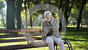 Old thoughtful man playing chess in park alone, social security for pensioners photo