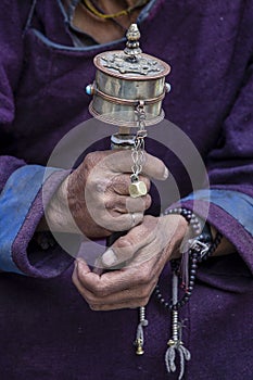 Old Tibetan woman holding buddhist prayer wheel in Hemis monastery, Ladakh, India. Hand and prayer wheel, close up