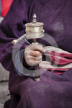 Old Tibetan woman holding buddhist prayer wheel in Lamayuru Gompa, , Ladakh, India.