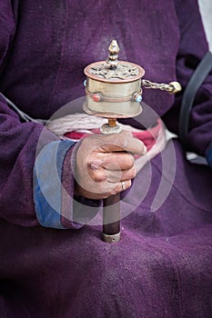 Old Tibetan woman holding buddhist prayer wheel in Lamayuru Gompa, , Ladakh, India.