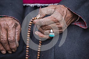 Old Tibetan woman holding buddhist rosary in Hemis monastery, Ladakh, India. Hand, turquoise ring and rosary, close up