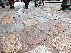 Old tiles on pavement and feet of pedestrians