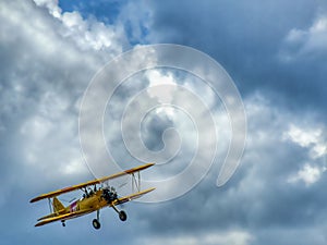 Old yellow biplane aircraft on colorful cloudy sky.