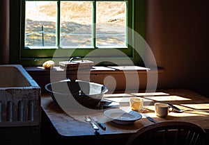 Old times farmhouse interior in a kitchen. Rural home kitchen with worn wooden table and mixing bowl, spoon, fork, plate