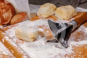 An old tool with a knife for making chopped dough for Napoleon cake. Wooden background with scattered flour, rolling pin