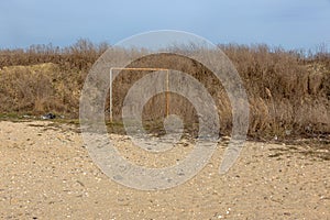 Old torn rusty football goal on an empty sandy beach. The concept of nostalgia. Old soccer goal in the field